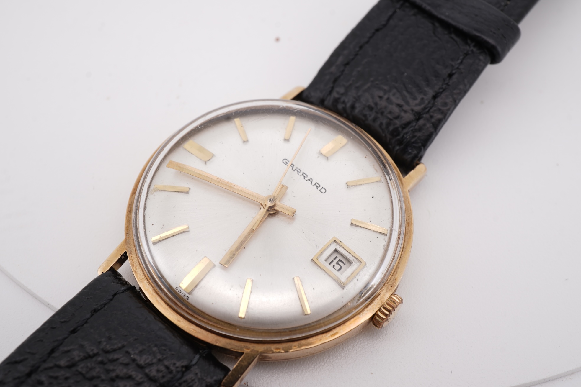 A gentleman's yellow metal Garrard manual wind wrist watch, with baton numerals and date aperture, case diameter 34mm, on a black leather strap.